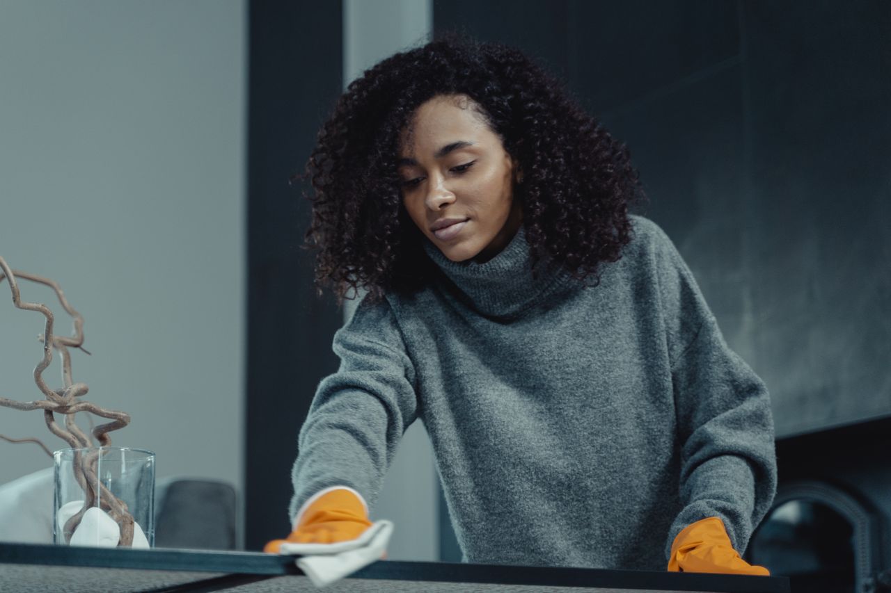 Une femme en pull gris nettoie une table avec soin, illustrant le ménage à domicile dans un cadre confortable.